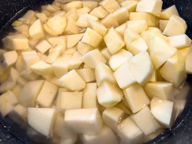 Koyu bir kasenin içinde suya batırılmış patateslerin yakın plan görüntüsü. Eşit kesilmiş patates parçaları çerçeveyi doldurarak soluk renklerini ve pürüzsüz dokularını gösteriyor. Işıklar tazeyi vurguluyor.