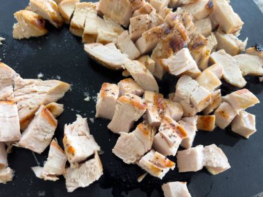 Küp küp tavuk göğsü koyu renk bir kesim tahtasına yerleştirilir. Tavuk, gözle görülür ızgara izleri ve sulu bir dokuyla eşit derecede pişirilir. Sahne, doğal bir mutfakla aydınlık.