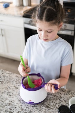 Odaklanmış bir dikkatle, bu filizlenen aşçılık sanatçısı krakerleri erimiş çikolataya batırarak iyi aydınlatılmış bir ev mutfağının sıcaklığında tatlı tatlar yaratıyor..