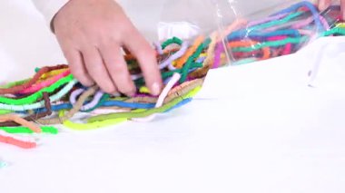 Eller titizlikle çok renkli, desenli kil boncuklardan oluşan bir kaleydoskop organize eder. Karmaşık bir şekilde sarmalanır ve beyaz bir zemin üzerine serilir..