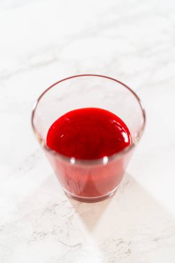 Tamamlanmış ahududu püresi berrak bir bardağa döküldü, Paskalya Kurabiyesi Sandviçi için canlı bir malzeme, ahududu kremalı..