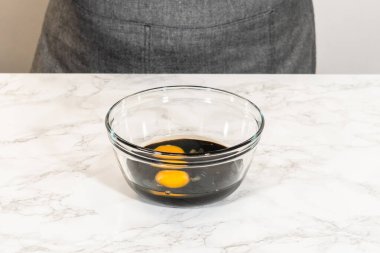 Üzüm pekmezi ve iki büyük yumurta içeren cam kasenin yakın plan görüntüsü. Baharatlı zencefilli kurabiye için mükemmel hamur. Koyu renkli pekmez, parlak yumurta sarılarıyla zıt düşer.