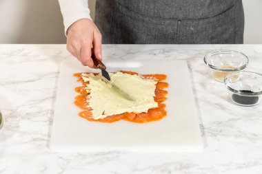 Krem peynir füme somon dilimlerinin üzerine eşit olarak yayılarak rulo için pürüzsüz bir taban oluşturur..