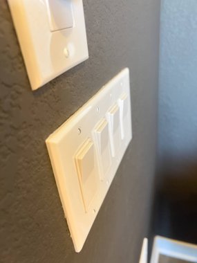 Koyu renkli bir duvara monte edilmiş iki beyaz düğmeye yakın plan. Görüntü, kıtır anahtar levhası ile desenli yüzey arasındaki kontrastı yakalar..