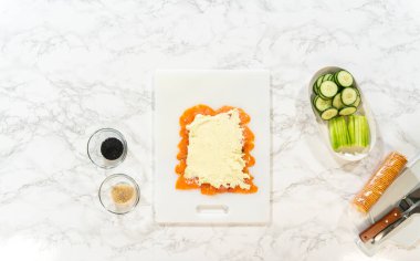 Krem peynir, kesme tahtasındaki füme somon dilimlerinin üzerine eşit olarak yayılarak dev ekmekler için pürüzsüz bir katman oluşturuyor..