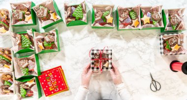 Noel kurabiyesinin hediye kutusunu saran, güzelce hazırlanmış Noel kutuları ile çevrili, tepeden tırnağa bir el resmi. Sahnede zencefilli kurabiye, şenlikli ambalajlar ve