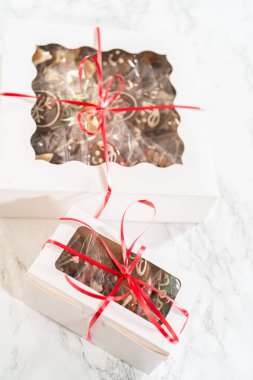 Bir el, canlı kırmızı bir kurdeleyle bağlanmış güzel paketlenmiş tatil kurabiyesi kutusunu tutar. İçerde, çeşitli dekore edilmiş zencefilli kurabiyeler temiz pencereden içeri bakıyor ve bunu yenilebilir mükemmel bir hediye yapıyor.