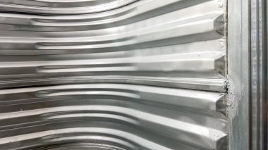 Interior view of a full metal corrugated window well wall, curving around the frame and forming a rigid, protective enclosure for basement safety access.