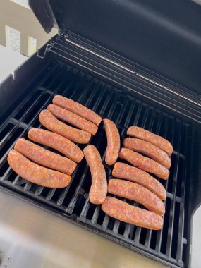 Sosisler barbekü ızgarasında kapağı açık, daha yeni kahverengileşmeye başladı. Açık hava manzarası yaz pikniğinin başladığını gösteriyor..