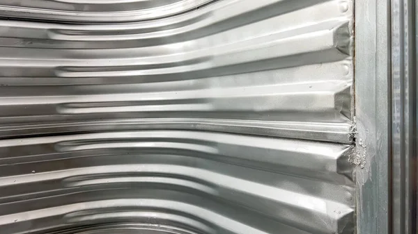 Çerçevenin etrafında kıvrılan ve bodrum katının güvenlik erişimi için katı, koruyucu bir muhafaza oluşturan tam metal eğimli pencere kuyusu duvarının iç görünümü.