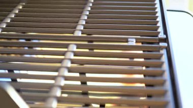 Yakından bakıldığında, banliyödeki bir evin balkonunda ilk açık hava yemek pişirme macerasını bekleyen iki ocaklı ızgaranın bozulmamış ızgarasını gösteriyor..