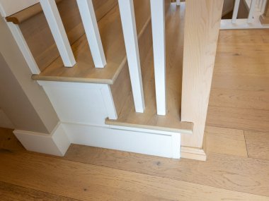 İç çekimde beyaz boyanmış korkuluklu ve ahşap döşemeli bir merdiven tabanı görünüyor. Parlak ışıklandırma işçiliği ve modern ev iç tasarımını ön plana çıkarıyor.