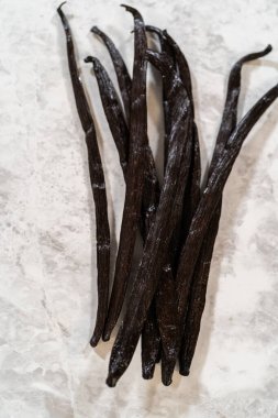 Birkaç vanilya çekirdeği parlak desenli taş yüzeyde gevşek bir tomar oluşturur. Doğal ışık, koyu renklerini ve ince parıltılarını vurgular..