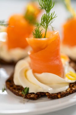 Çıtır bir krakerin üzerine zarif bir şekilde yerleştirilmiş füme somon kanalı. Üstünde krem peyniri, taze kekik ve zeytinyağı var. Canlı portakal somonu kontrastları