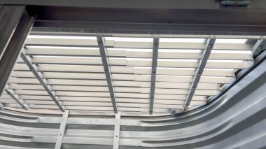 Yukarıdaki güvenlik ızgarasından ışık saçan metal bir pencerenin içi. Bükülmüş metal dokuyu ekler ve temiz, parlak ışığı yansıtır..