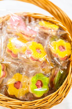 Colorful flower-shaped Easter cookie sandwiches with raspberry buttercream filling, individually wrapped and arranged in a wicker basket. Perfect for spring gifting, Easter parties, and festive