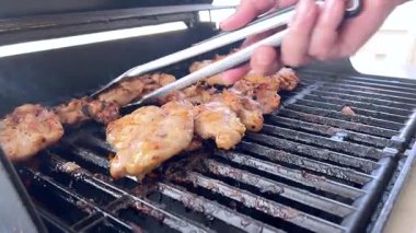 Salamura edilmiş tavuk butları küçük bir Weber ızgarasının ızgarasında cızırdar, havayı iştah açıcı bir koku ve hafif bir dumanla doldurur..