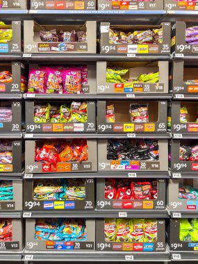 Parker, CO, ABD-19 Eylül 2025 - Cadılar Bayramı şekerleriyle dolu parlak ambalajlı bir mağaza rafı. Renkli çantalar sergilenen floresan ışıkların altında. Görüntü