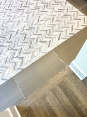 Modern bir banyonun yakın çekimde, kahverengi bir fayansla birleşen sembol desenli fayans duvarını gösteriyor. Yumuşak ışıklandırma, ahşap zeminin bir parçasıyla fayansların dokusunu ve kontrastını arttırır..