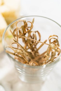 Dekoratif bambu sandviç kazmaları, mini salatalıklı sandviçleri hazırlamak ve servis etmek için kullanılan temiz bir içecek bardağına dizilmiş. Gıda tasarım araçları veya olay hazırlama için kullanışlı bir depolama resmi