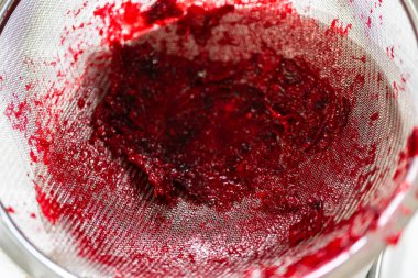 İnce bir süzgeçten geçen taze kızılcık sosunun yakın plan çekimi. Zengin, yakut kırmızısı sos elek içinde görülebilir, canlı sıvı hamurdan ayrılır. Bu işlem
