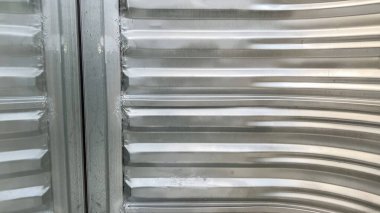 Görünürde dikey çıkıntıları olan boş bir çelik pencerenin düz bir görüntüsü. Işıklandırma doğal ve hatta metal yüzeyinin endüstriyel dokusu ve temiz çizgilerini vurguluyor..