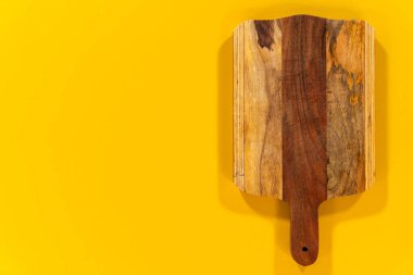 Saplı ahşap bir kesme tahtası parlak sarı bir arka plan üzerine kuruludur. Resim ahşap tonları ve tahtanın el yapımı görünümünü vurgular.