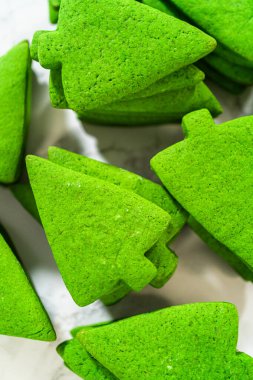 Bir yığın sade yeşil Noel ağacı kurabiyesi, canlı yeşil rengini ve pürüzsüz dokusunu vurguluyor.