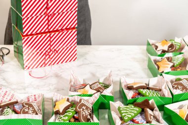 Orta menzilli çekimler bir dizi Noel kurabiyesi hediye kutularını düzgünce bir masanın üzerinde sergiliyor. Her yeşil kutu süslü zencefilli kurabiyelerle dolu, eldivenler de dahil.