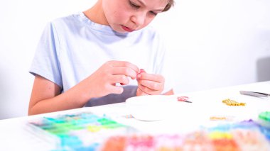 Genç bir kızın narin parmakları parlak, renkli boncuklardan oluşan bir hazinede geziniyor. Her bölümde seçilecek yeni bir renk var. Neşeli bir vazifeye daldı.