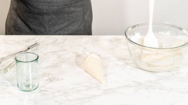 Simple White Royal Icing hazırlığı için hazırlanmış cam bir kavanoz taze çırpılmış kremayla dolu bir karıştırma kabının yanına kurulmuş..