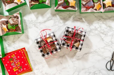 Noel kurabiyesinin hediye kutusunu saran, güzelce hazırlanmış Noel kutuları ile çevrili, tepeden tırnağa bir el resmi. Sahnede zencefilli kurabiye, şenlikli ambalajlar ve