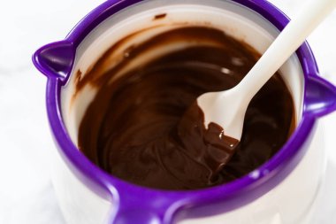 Erimiş çikolatayı eritme kabında eritilmiş olarak Spatula Tarifi ile yakın çekim: Erimiş çikolatanın mor bir eritme kabında bir spatulayla karıştırılması, Çikolata Royal için pürüzsüz bir tutarlılık sağlar