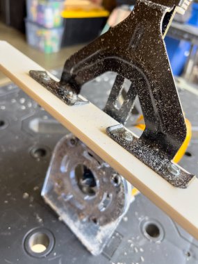 Yönlendirici alet siyah bir masanın kenarındaki beyaz ahşap şeridi buduyor. Görüntü devam eden bir atölye sürecini yakalıyor.