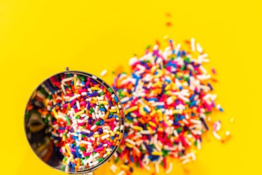 Kalp şeklinde şeker serpiştirme düzeneği. Üstünde metal bir kepçe var. Temiz sarı bir zemin üzerine kurulmuş..