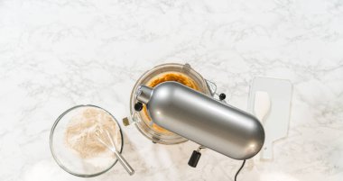 Büfe mikserinin genel manzarası ve karıştırılmaya hazır Amber Zencefilli Kurabiye Hamuru için malzemeler. Kuru ve ıslak malzemeler mikserin etrafına mermer bir yüzey üzerine dizilir..