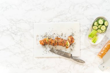 Tütsülenmiş somon krem peynirli rulo siyah ve beyaz susam tohumlarıyla kaplı, kesme tahtasının üzerinde bir bıçakla sergileniyor..