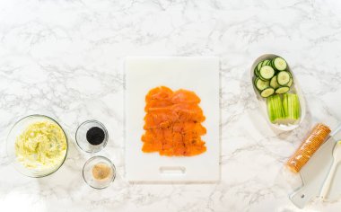 Tütsülenmiş somon dilimleri bir kesme tahtasına güzelce dizilir, krem peynirle ve jumbo rulo için diğer malzemelerle tabakalandırılmaya hazırdır..