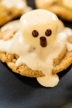 Karanlık arka planda hayalet şekilli kremayla kaplı tek bir kurabiyenin yakın görüntüsü. Yumuşak ışıklandırma krema detaylarını ve pişmiş kurabiye yüzeyini vurgular.