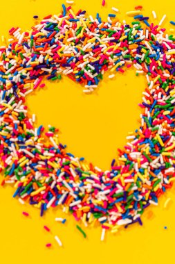 Parlak gökkuşağı renginde serpiştirilmiş kalp şeklinde parlak sarı dikey arka plan. Görüntü, neşeli ve neşe dolu bir estetiği vurgulayarak yakından kırpılmış ve iyi aydınlatılmış..
