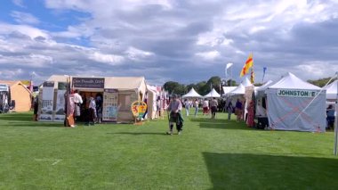 Sedalia, CO, Usa-September 20, 2025 - Slow Motion - Bir açık hava festivalinde beyaz çadırlar ve renkli klan afişleriyle dolu çimenli bir yürüyüş yolunun geniş açılışı. İnsanlar yol boyunca kısmen yürür