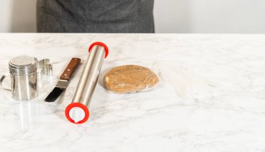 Amber zencefilli kurabiye kurabiyeleri için soğutulmuş hamur topunun yan perspektifi mermer bir yüzeyde merdane iğne ve kurabiye kesicilerin yanında oturuyor..
