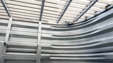 Pencerenin içinden açılı görüntü üst güvenlik ızgarasını ve dikey merdiven parmaklıklarını gösteriyor. Bükülmüş metal duvarlar tekrar eden dokular ve minimum endüstriyel bir his yaratıyor..