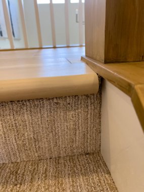 Beyaz bir duvar süpürgeliği ve doğal ahşap döşeme ile buluştuğu tek bir halı basamağının ayrıntılı görüntüsü. Materyal karşıtlık gösterileri ya da iç yapı görüntüleri için mükemmel.