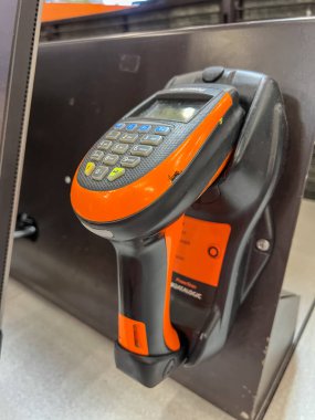 Parker, Colorado, ABD-1 Ağustos 2025 - Bir kenetlenme istasyonuna monte edilmiş turuncu ve siyah bir barkod tarayıcısının yakın görüntüsü. Tarayıcı dikey olarak konumlandırılmış ve kapalı alan tarafından aydınlatılmış.