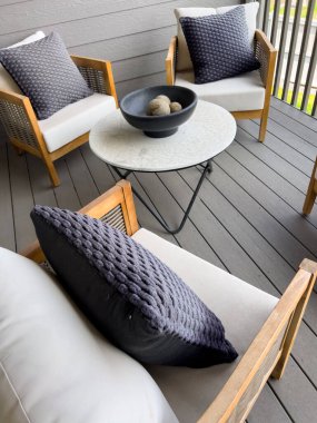 Yastıklı sandalyelerin ve yuvarlak bir sehpanın birleşik ahşap güvertede durduğu modern bir teras seti. Nötr renk paleti ve çağdaş tasarım açık havada rahat bir yaşam alanı oluşturur.