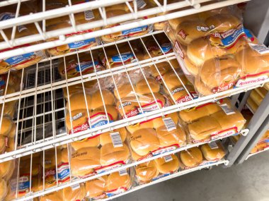 Parker, Colorado, ABD-20 Haziran 2025 - Depoda paketlenmiş hamburger çörekleri ve sosisli sandviçlerle dolu market raflarının yakın çekimi. Ekmek, parlak iç mekanların altında düzenli olarak düzenlenir.