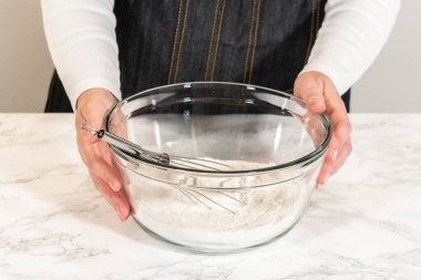 Elinde mermer tezgahın üzerinde un dolu cam bir karıştırma kabı tutan kişi. Yumuşak ışıklandırma ve nötr tonlar temiz ve profesyonel pişirme ortamı yaratır.