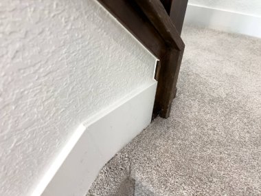 Bir merdivenin dibinde bej halı buluşmasının ayrıntılı görüntüsü. Sahne, konut iç tasarımında maddi kontrastı vurguluyor.