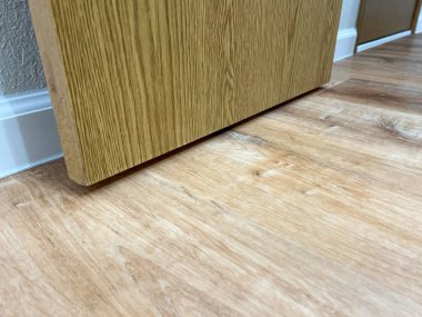 Ahşap mutfak dolabının alt tarafındaki ahşap döşemeye yakın bir görüntü. Ahşap tonlar kapalı mekan ışıklarının altında ince bir tezat oluşturuyor. Bir süpürgelik ve duvar bölümü